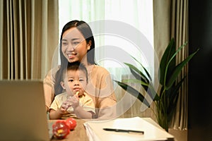 Shot of a young mother having video call with her clients over laptop and carrying her baby on laps