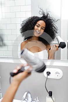 Shot of a young woman blowdrying her hair