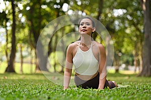 Shot of young woman doing yoga in high cobra asana pose on green grass. Yoga, meditation and healthy lifestyle concept