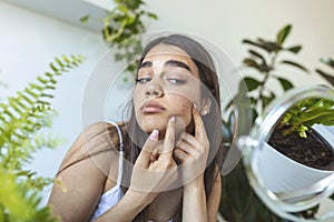 Shot of a young woman squeezing a pimple in front of the mirror, A young woman looking shocked as she examines her skin