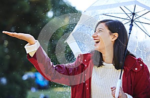 Its raining down hard. Shot of a young woman standing in the rain with an umbrella.