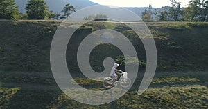 Shot of a young womanin a light dress and hat riding bicycle on rural road