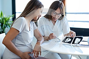 Young woman gynecologist doctor showing to pregnant woman ultrasound scan baby in medical consultation