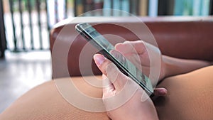 Shot of a young women hands typing something on a touchscreen of a smart phone in the living room