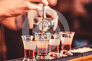 Shots at the nightclub. Red alcoholic drink in glasses on bar. Red cocktail at the nightclub. Barman preparing cocktail