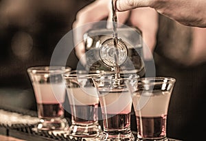 Shots at the nightclub. Red alcoholic drink in glasses on bar. Red cocktail at the nightclub. Barman preparing cocktail