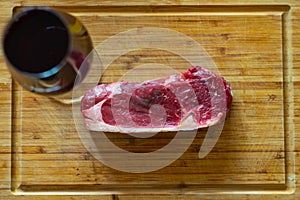 Shots of a sliced raw fresh  rump steak with fat on the steak on a wooden board and a glass of wine