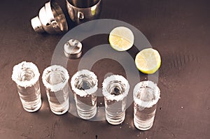 Shots of tequila and pieces of lime and shaker/shots of tequila and pieces of lime and shaker on a dark background. Top view