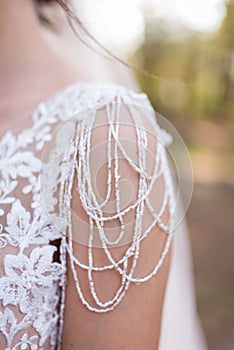 On the shoulder of the bride wakes a piece of a wedding dress with a lot of beads. .