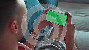 Shoulder shot of a Man's Hand Holding horizontal Green Mock-up Screen Smartphone. Modern Mobile Phone. In the