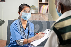 Shoulder shot, young doctor or nurse writing prescription during home visiting to sick senior man while both worn face
