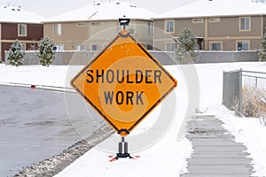 Shoulder Work sign on the snowy sidewalk of road under construction in winter