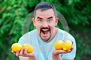 Shouting man holding in hands four yellow lemons. Man with wide open mouth standing outdoor with citrus fruits