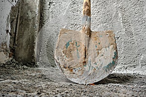 Shovel in front of the recently made plastered wall by concrete.