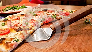 Shovel with a slice of delicious Italian pizza on a wooden board in a restaurant on a served table