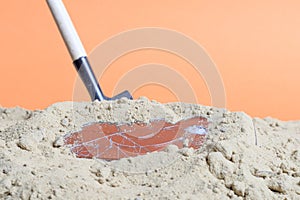 A shovel stuck in the sand there is a broken smartphone
