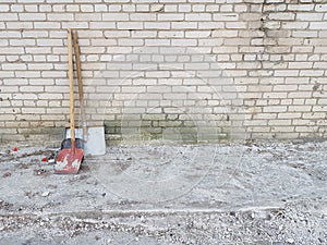 3 shovels of different colors and shapes stand against a brick wall.