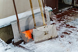 Shovels and scrapers for snow removal stand near the wall