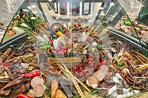 Showcase with an abundance of assortment of sausages and meat prepared products, cheese, fruit, wine