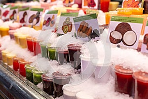 Showcase with different types of colorful cold juice and smoothie in the ice on the market in Barcelona, Catalonia