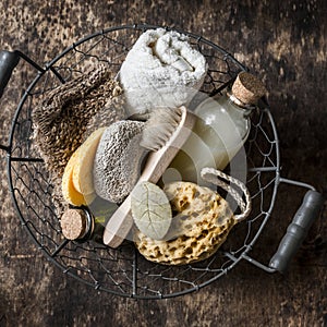 Shower accessories in vintage basket - shampoo, sponge, soap, facial brush, towel, washcloth, pumice stone. On wooden background