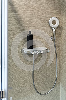 Shower cabin. Decorative beige wall and shower head. Black bottle of shampoo. Modern bathroom design