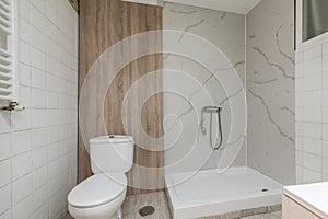 Shower cabin without screens in a bathroom with white marble-like walls and a wooden panel