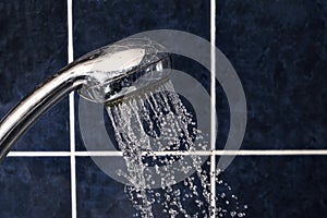 Shower head on tiled background with stream of water drops flying out, copyspace