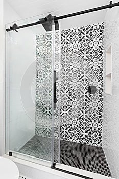 A shower with a sliding door and black and white tiles.