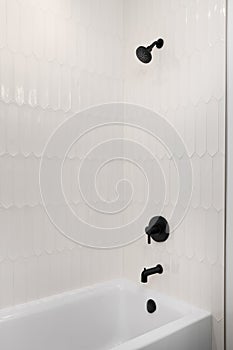 A shower with tan picket tiles and black showerhead.