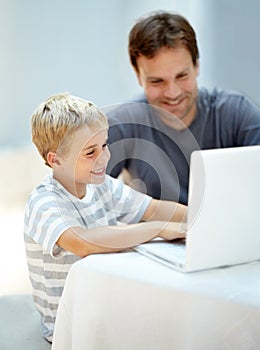 Showing dad a thing or two. Young boy on his laptop with his father next to him.
