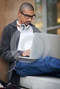 Showing dedication to his education. a college student using his laptop while sitting outside at campus.