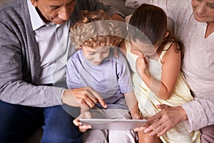Showing granny and gramps the latest tech. A shot of two kids and their grandparents using a digital tablet while