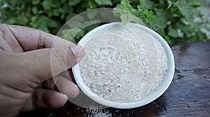 Showing Psyllium husks on a white small plastic bowl with hand top view