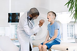 Showing throat. Little boy opening mouth showing her throat while visiting young handsome African man doctor in his