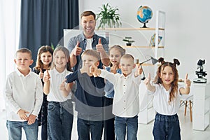 Showing thumbs up. Group of children students in class at school with teacher
