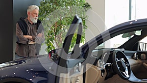 Showroom car, old man examining automotive for sale at the dealership Spbi. Male client with crossed