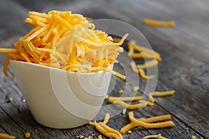 Shredded cheddar cheese in white cup close up view