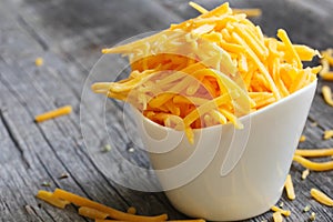 Shredded cheddar cheese in white cup close up view