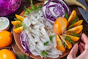 Shredded red cabbage, daikon radish and yellow tomatoes with dill in clay bowl on black background