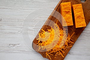 Shredded Sharp Cheddar Cheese on a rustic wooden board on a white wooden background, top view. Flat lay, overhead, from above.