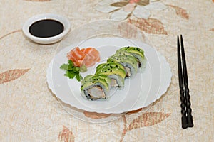 Shrimp and avocado rolls on a white plate with salmon decoration, soy sauce and black chopsticks in rustic table.