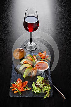 Shrimp dish with apples, lettuce, tomatoes, herbs, freshly baked bun and a glass of red wine