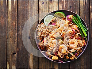 Shrimp pad thai on plate in flat lay composition with copy space atop rustic wooden table photo