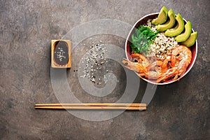 Shrimp poke bowl, rice, avocado, chuka, soy sauce and sesame on a dark rustic background. Top view, flat lay, copy space