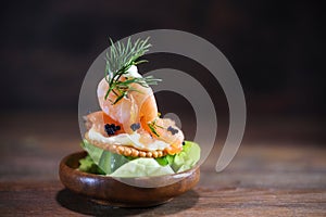 Shrimp, salmon and caviar on a cracker with mayonnaise in a small wooden bowl on a dark rustic background, snack for a holiday