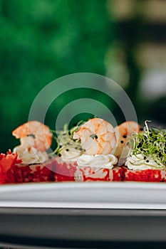 Shrimp sushi on a white plate decorated with caviar, greens and shrimp