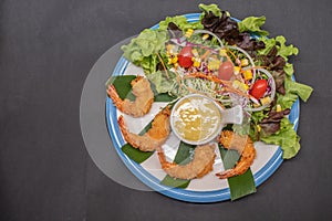 Shrimp tempura and salad of fresh vegetables close-up on a plate on black background. horizontal view from above