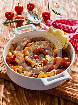 Shrimps in white baking dish on wooden background. Baked with cherry tomatoes and feta cheese