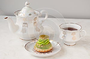Shu cake with pistachio cream and a white tea set on the table